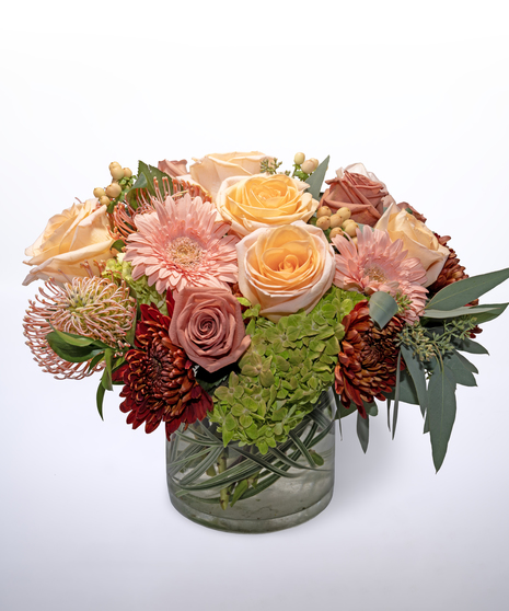hydrangea, peach roses, pink gerbera daisies and peach protea, with hypericum berries and seeded eucalyptus in a clear vase