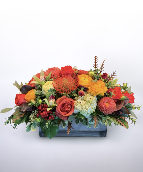 hydrangea, sunflowers, orange dahlias, orange calla lilies, orange and yellow roses and protea in a green pot